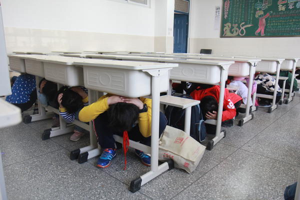 警报响起，学生迅速蹲下，双手抱头躲在课桌旁边
